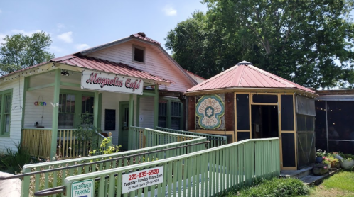 A charming café with a colorful sign, featuring a porch and a unique round structure with a decorative design.