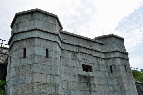 Stone structure with two towers, featuring an inscription that reads "ERECTED 1892," against a cloudy sky.