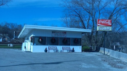 A small, white restaurant with a Coca-Cola sign, decorated for the holidays, set against a clear blue sky.