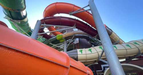 Colorful water slides twist and turn against a clear blue sky, with a mix of orange, red, green, and beige sections.