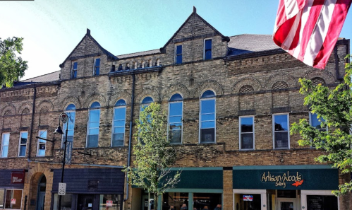 Historic brick building with arched windows, featuring shops below and an American flag in the foreground.