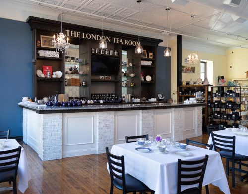 A cozy tea room with a stylish bar, elegant tables, and shelves filled with tea and accessories.
