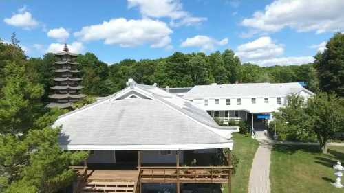 Aerial view of a building with a pagoda-style structure surrounded by trees and a pathway under a blue sky.