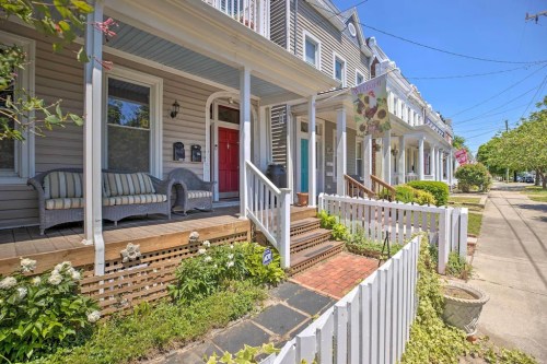 Charming row of houses with porches, white picket fences, and lush greenery on a sunny day.