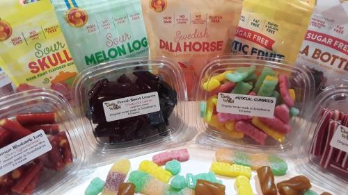 Colorful assortment of gummy candies in various shapes and flavors, displayed in clear containers and bags.