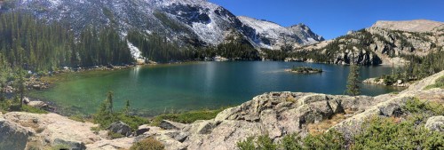 A serene mountain lake surrounded by rocky shores and lush greenery, with snow-capped peaks in the background.