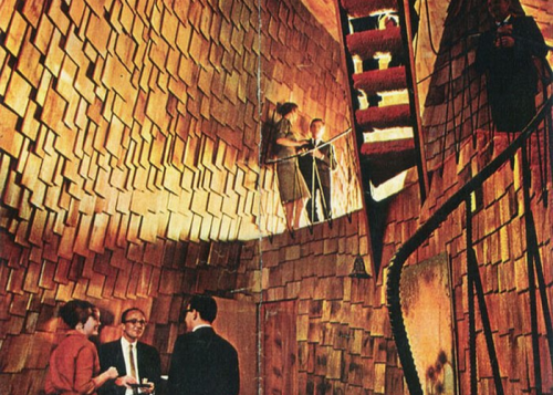 A retro interior with wooden walls, featuring people conversing and a spiral staircase in a unique architectural space.