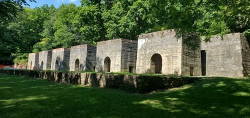 Abandoned stone structures with arched entrances, surrounded by lush greenery and trees.