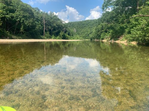 A serene river scene with clear water reflecting blue skies and lush green trees along the banks.