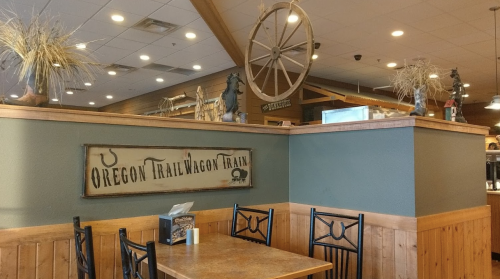 Interior of a restaurant featuring wooden decor, a wagon wheel, and a sign that reads "Oregon Trail Wagon Train."