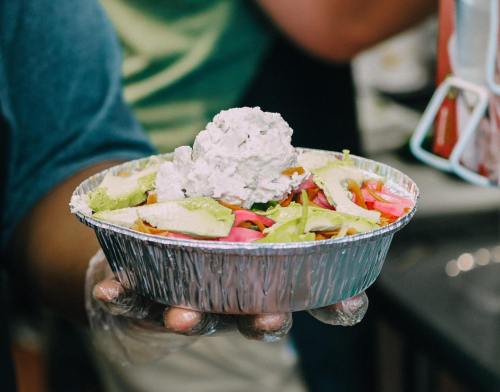 A person holding a silver bowl filled with a colorful salad topped with a dollop of creamy dressing.