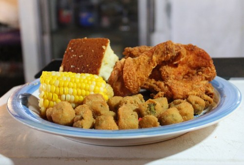 A plate of fried chicken, cornbread, corn on the cob, and fried okra, served with a side of mashed potatoes.