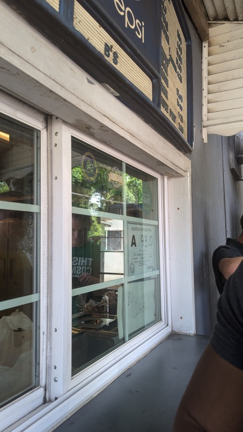 A view of a food service window with a menu above and a person preparing an order inside.