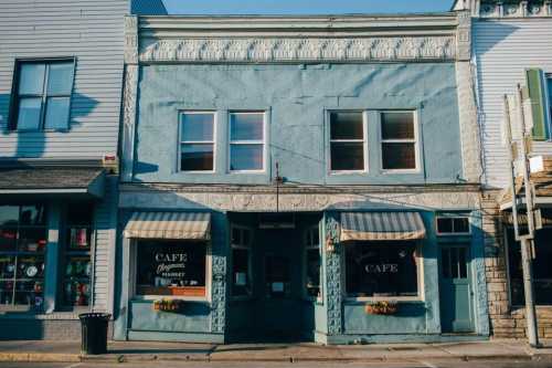 A charming blue cafe with decorative trim, featuring large windows and striped awnings, set in a quaint street.