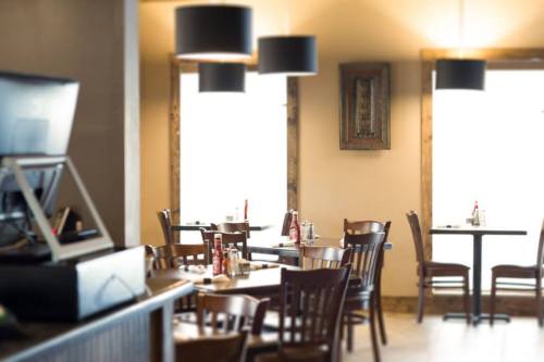 Cozy restaurant interior with wooden tables, chairs, and pendant lights, featuring ketchup bottles on the tables.