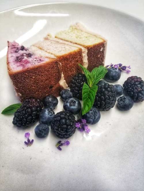 Three slices of cake on a plate, surrounded by fresh blueberries, blackberries, and mint leaves.