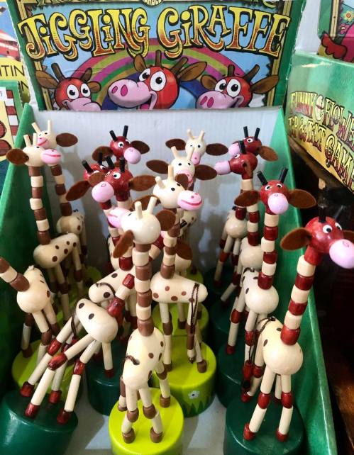 A colorful display of wooden giraffe toys with playful designs, arranged in a green box labeled "Jiggling Giraffe."