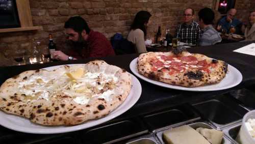 Two pizzas on white plates, one topped with cheese and lemon, the other with pepperoni, in a cozy restaurant setting.