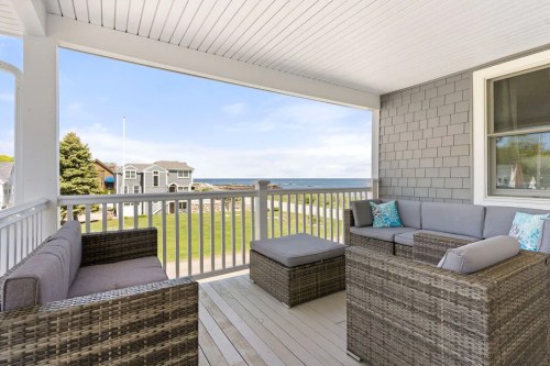 A cozy porch with wicker furniture overlooks a scenic view of the ocean and nearby houses.