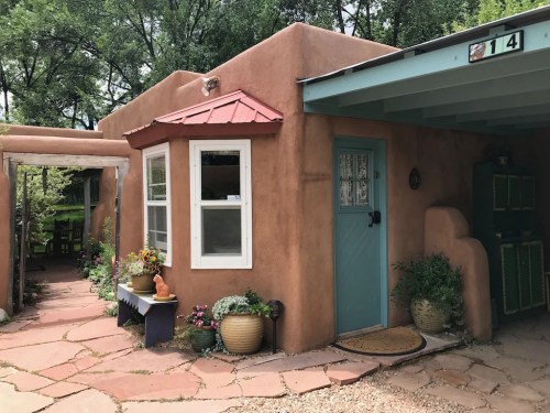 A charming adobe-style home with a red roof, blue door, and a stone pathway lined with potted plants.