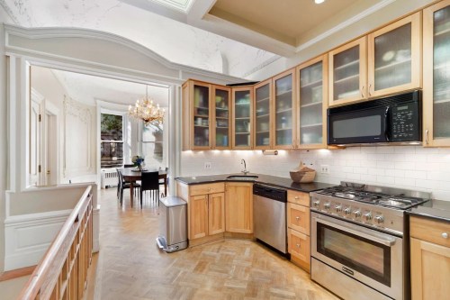 Bright kitchen with wooden cabinets, stainless steel appliances, and a view into a dining area with a chandelier.