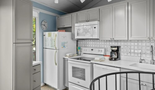 A modern kitchen featuring light gray cabinets, white appliances, and a tiled backsplash. Natural light from a window.