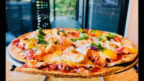 A freshly baked pizza topped with cheese, vegetables, and herbs, served on a round tray.