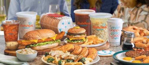 A table filled with various dishes, including sandwiches, fries, pasta, and drinks, showcasing a variety of comfort food.