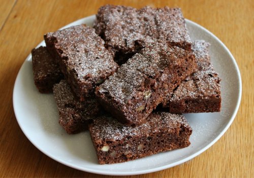 A plate of chocolate brownies dusted with powdered sugar, arranged neatly on a wooden table.