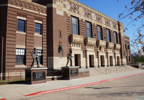 Historic building with decorative brickwork and two statues of musicians at the entrance, under a clear blue sky.