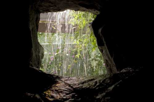 A view through a rocky opening, showcasing cascading water and lush greenery beyond.