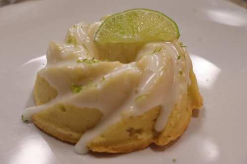 A small lime bundt cake topped with creamy frosting and a slice of lime on a white plate.
