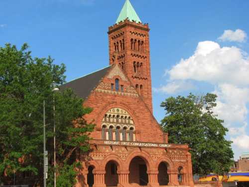 Historic First Congregational Church, featuring red brick architecture and a green-topped tower, surrounded by trees.