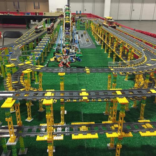 A colorful model train layout made of building blocks, featuring tracks, bridges, and a vibrant green base.