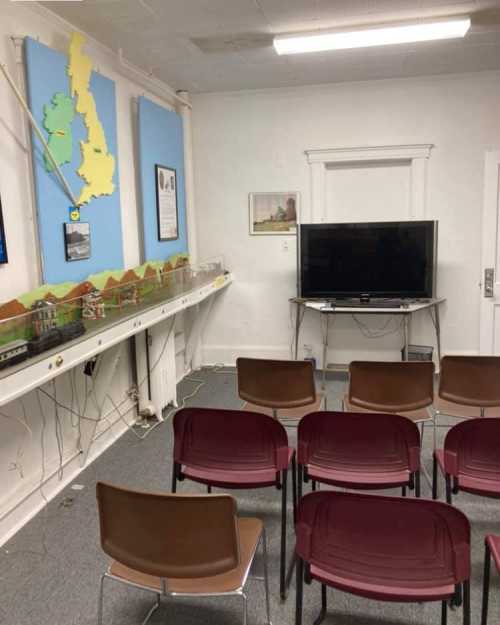 A room with a TV, chairs, and a wall map of the UK, featuring a display of model buildings on a table.