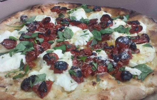 A close-up of a pizza topped with cheese, roasted tomatoes, herbs, and crispy pepperoni on a golden crust.