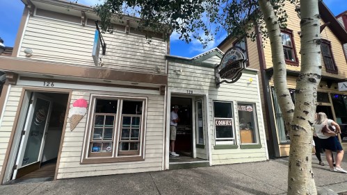 A quaint street scene featuring two shops, one with an ice cream sign and the other selling cookies, under a blue sky.