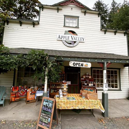A quaint store named "Apple Valley" with an open sign, featuring a display table and colorful decorations outside.