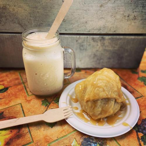 A mason jar filled with a creamy drink beside a plate of dessert drizzled with syrup on a colorful tablecloth.