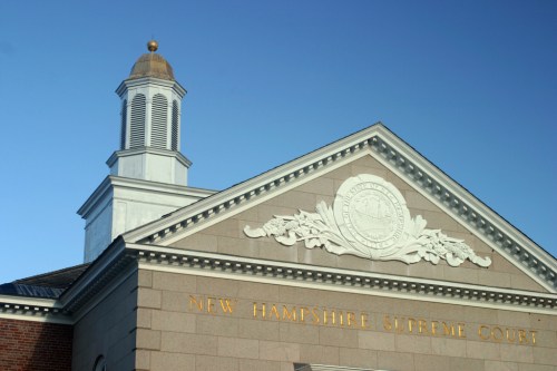 The facade of the New Hampshire Supreme Court building with a decorative emblem and clear blue sky.