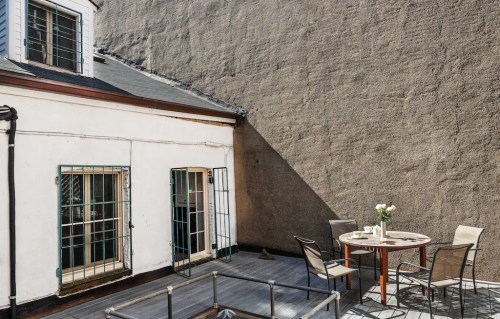 A small outdoor patio with a round table and chairs, surrounded by a gray wall and a white building.