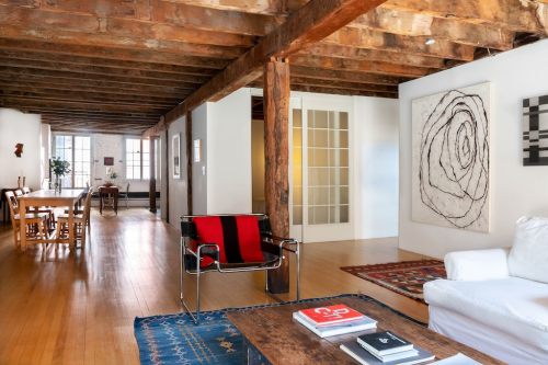 Spacious interior with wooden beams, a white sofa, and modern art, featuring a dining area and natural light.