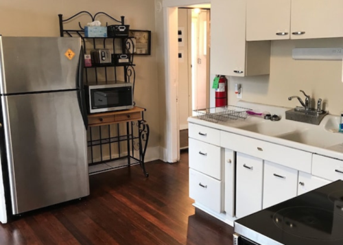A small kitchen featuring a stainless steel fridge, microwave, sink, and stove with wooden flooring.