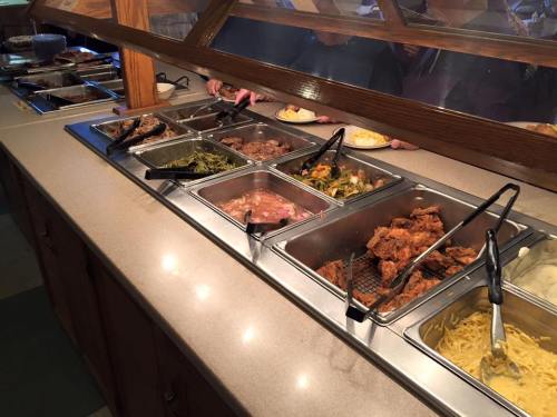A buffet with various dishes including meats, vegetables, and sides, served in metal trays with tongs.