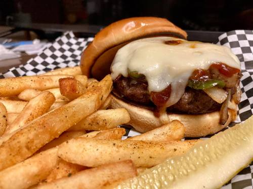 A juicy cheeseburger with melted cheese and toppings, served with crispy fries and a pickle on the side.