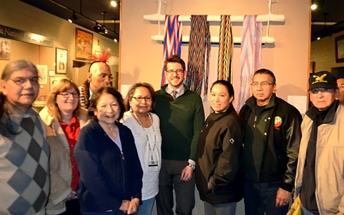 A group of diverse individuals poses together in an exhibit featuring colorful woven textiles.