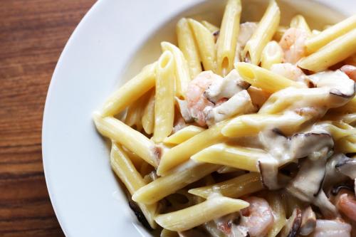 A close-up of creamy pasta with shrimp and mushrooms served in a white bowl on a wooden table.