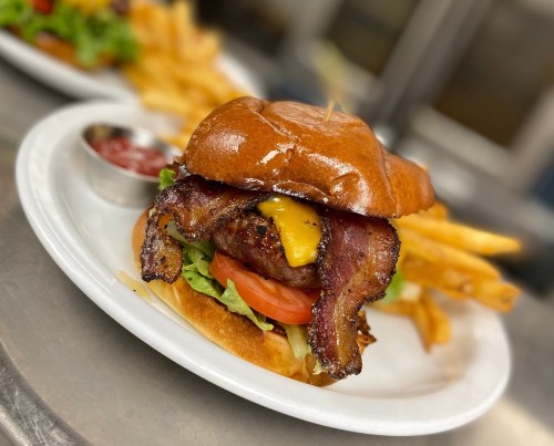 A juicy burger with bacon, cheese, lettuce, and tomato, served with fries and a side of ketchup on a white plate.