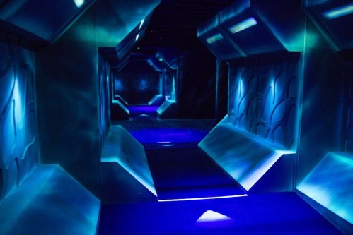 A futuristic hallway illuminated with blue lights, featuring textured walls and a glowing floor.