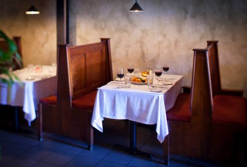 A cozy restaurant setting with a table for two, featuring wine glasses, a candle, and a plate of food.